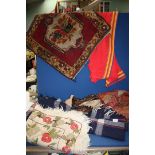 A box of material, navy blanket, burgundy throw, small carpet, embroidery rug etc.