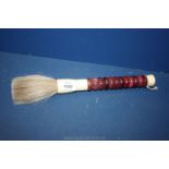 A bone handled horse hair fly swatter with burgundy marble decoration.