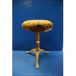 A heavy cast iron based three splay footed octagonal stool with leaf patterned velvet type