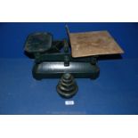 A large pair of weighing scales painted dark green with brass plate and five weights.