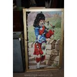 A framed rectangular carpet type picture of a highlander playing the bagpipes on battlements with