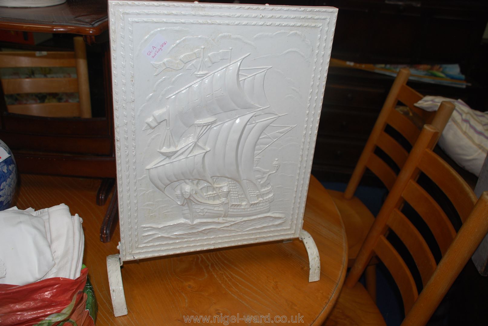 A metal embossed firescreen painted white, galleon detail.