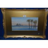 A gilt framed and mounted Watercolour depicting an Egyptian scene with pyramids and palm trees.