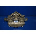 A heavy ornate brass pen stand with two inkwells and hinged lids and pen rest to front,