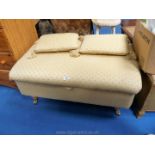 Low upholstered storage unit on brass casters with two matching cushions,