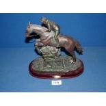 A reproduction of a horse and jockey jumping over a fence in resin,