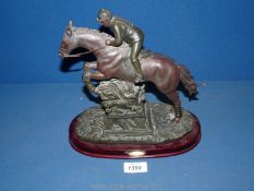 A reproduction of a horse and jockey jumping over a fence in resin,