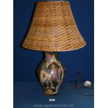 A tall ceramic table lamp with decoupage of Henry VIII, and a lion with wicker shade.