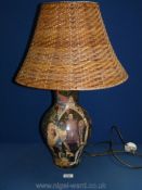 A tall ceramic table lamp with decoupage of Henry VIII, and a lion with wicker shade.