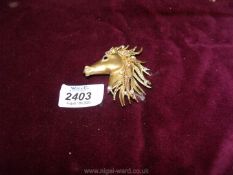 A gold metal brooch in the shape of a horses head with diamonte and a black stone for the eye.