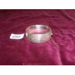 A silver bangle with scroll design, safety chain unattached.