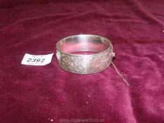 A silver bangle with scroll design, safety chain unattached.