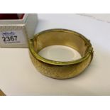 A boxed yellow metal hollow bangle with press action latch and safety chain and decorated with