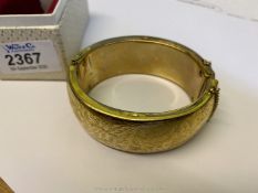 A boxed yellow metal hollow bangle with press action latch and safety chain and decorated with