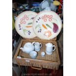 A wicker picnic basket, part tea service and two platters.