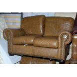 A tan twin sofa and two matching armchairs in leather with brass stud detail.