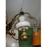 A brass oil lamp in a metal banjo style hanging frame.