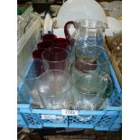 A tray with five cranberry glasses and jug with red handle and one other water jug with four large