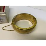 A boxed yellow metal hollow bangle with press action latch and safety chain and decorated with