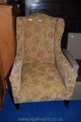 An Edwardian wing-back armchair nicely upholstered in a floral fabric and standing on tapering