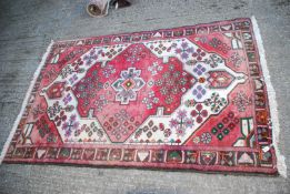 A bordered patterned and fringed Rug in red and cream with stylized flowers, some fading, 78" x 50".