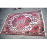 A bordered patterned and fringed Rug in red and cream with stylized flowers, some fading, 78" x 50".