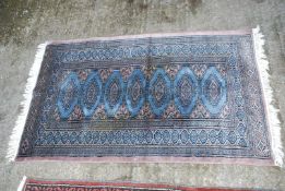 A small bordered patterned and fringed Rug in light blue and brown with hexagons down the centre,