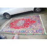 A large bordered patterned and fringed Rug in red, purple and green ground with flower vases design,