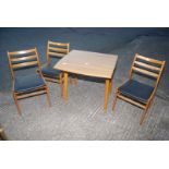 A drop-leaf wood-grain Formica topped kitchen table and three chairs.