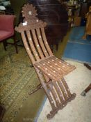 An unusual slatted Eastern hardwood folding chair decorated with blind fret-work/carved scroll-work