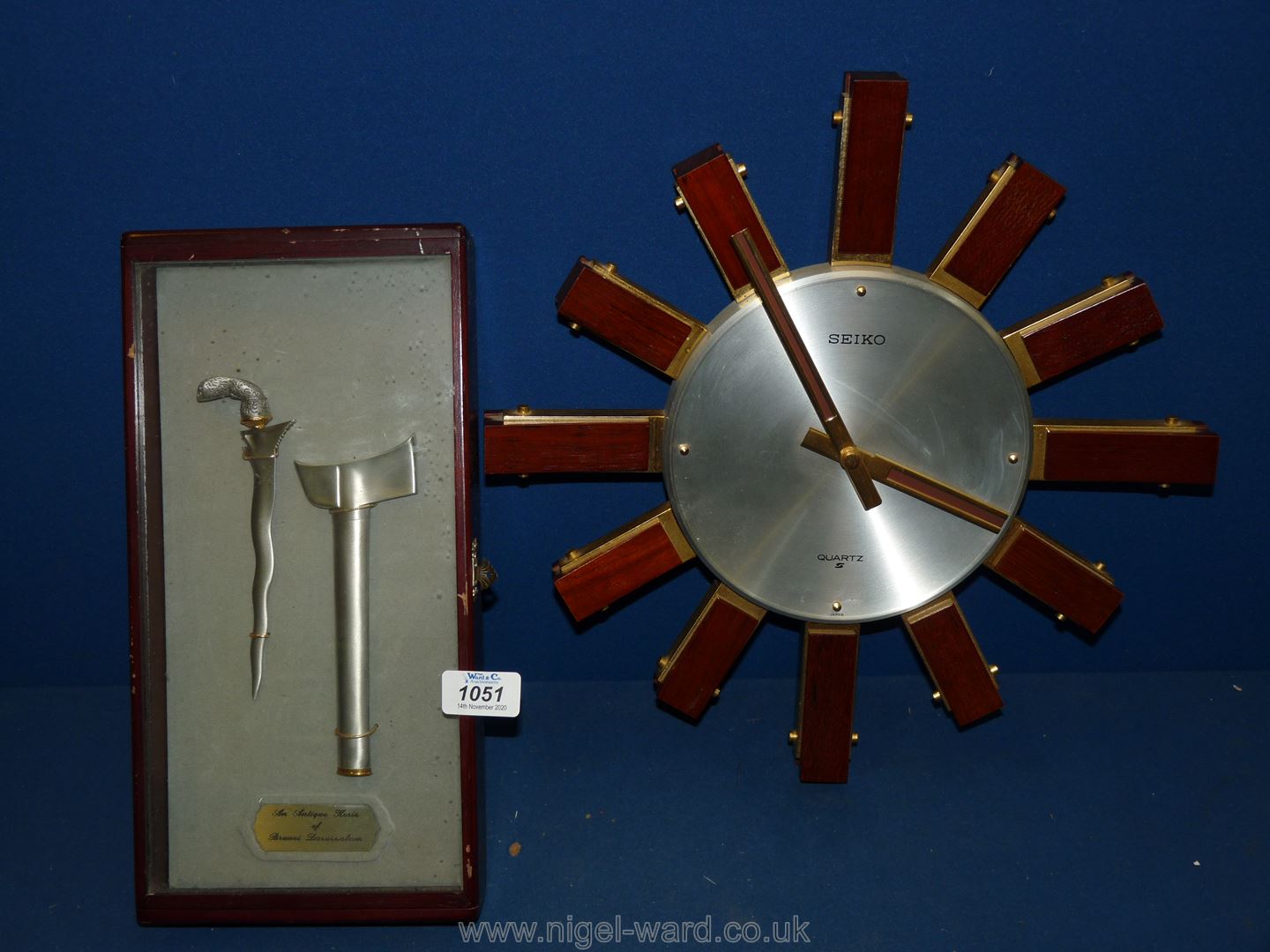 A dark-wood display case with hinged glazed lid containing a satin-finished metal miniature