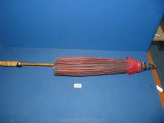 A red Japanese parasol with bamboo handle and colourful thread decoration to the interior.