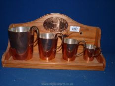 A graduated set of copper ale measures marked HMS to base with a wooden stand fitted with copper