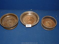 Three plated bottle coasters with wooden bases, two matching and one other.