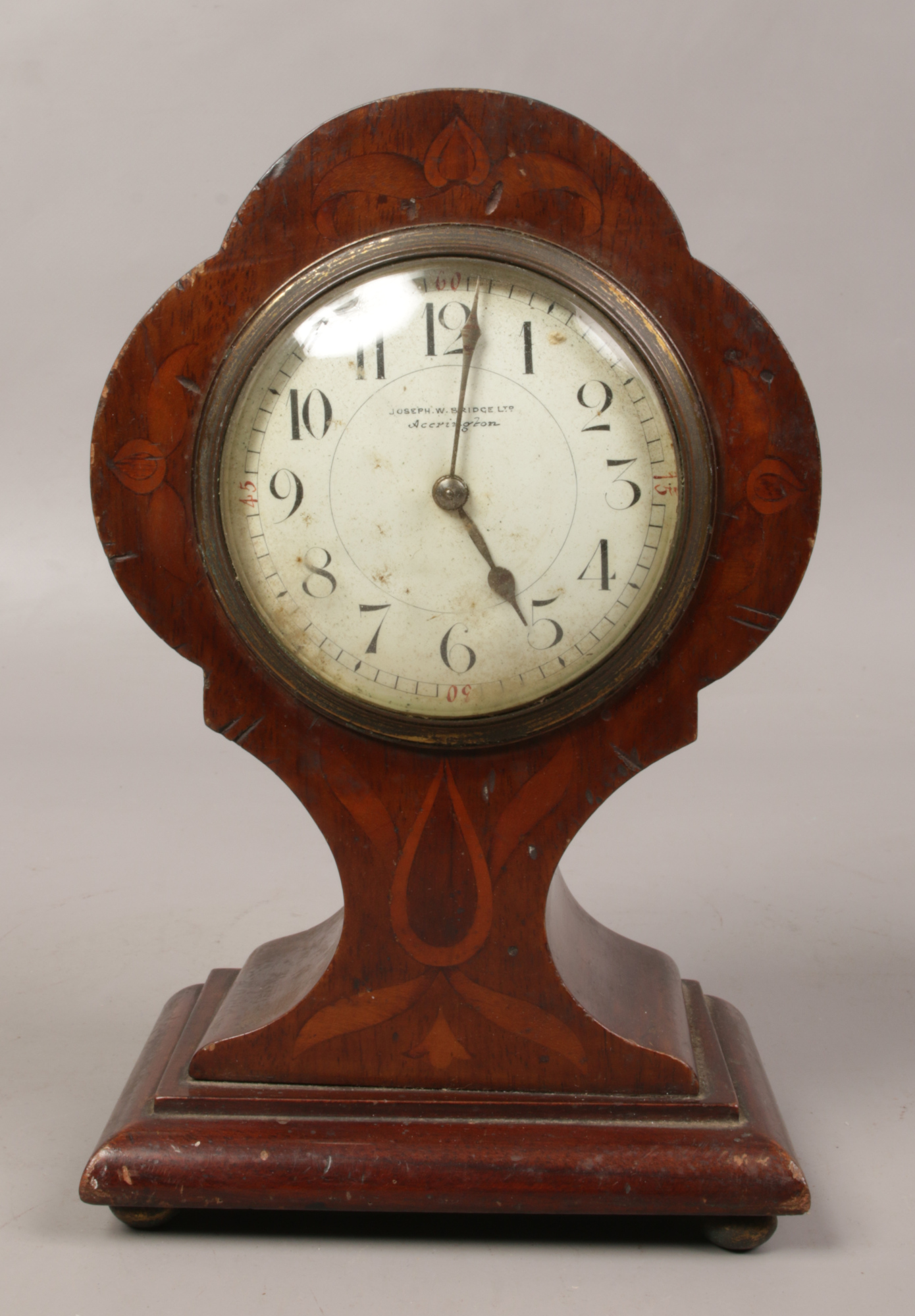 An Edwardian inlaid mahogany balloon mantel clock with cylinder movement and raised on ball feet.