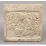 An Oriental carved stone square panel. Decorated in relief with a crouching figure collecting