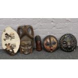 Four carved wooden African tribal masks to include beadwork example, along with a cowhide shield.