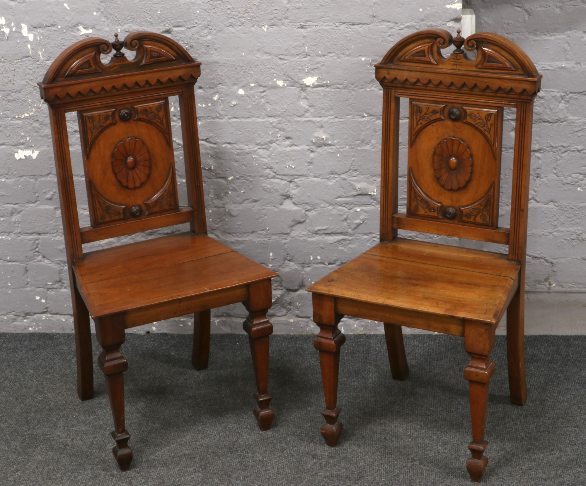A pair of Victorian carved mahogany hall chairs. With swan neck cresting rails and raised on