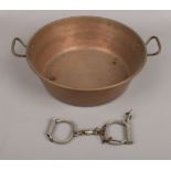 A pair of vintage metal police handcuffs along with a copper pan.