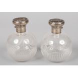 A pair of Edwardian silver mounted glass perfume bottles of globular form. The silver tops each with