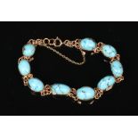 A gold mounted turquoise bracelet. With nine ovoid stones interlinked by a pair of chains.