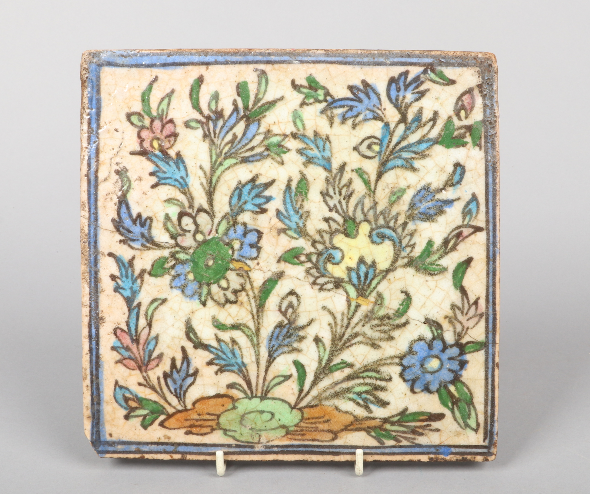 A 19th century Iznik square tile. Decorated with stylized flowers in polychrome enamels under a blue