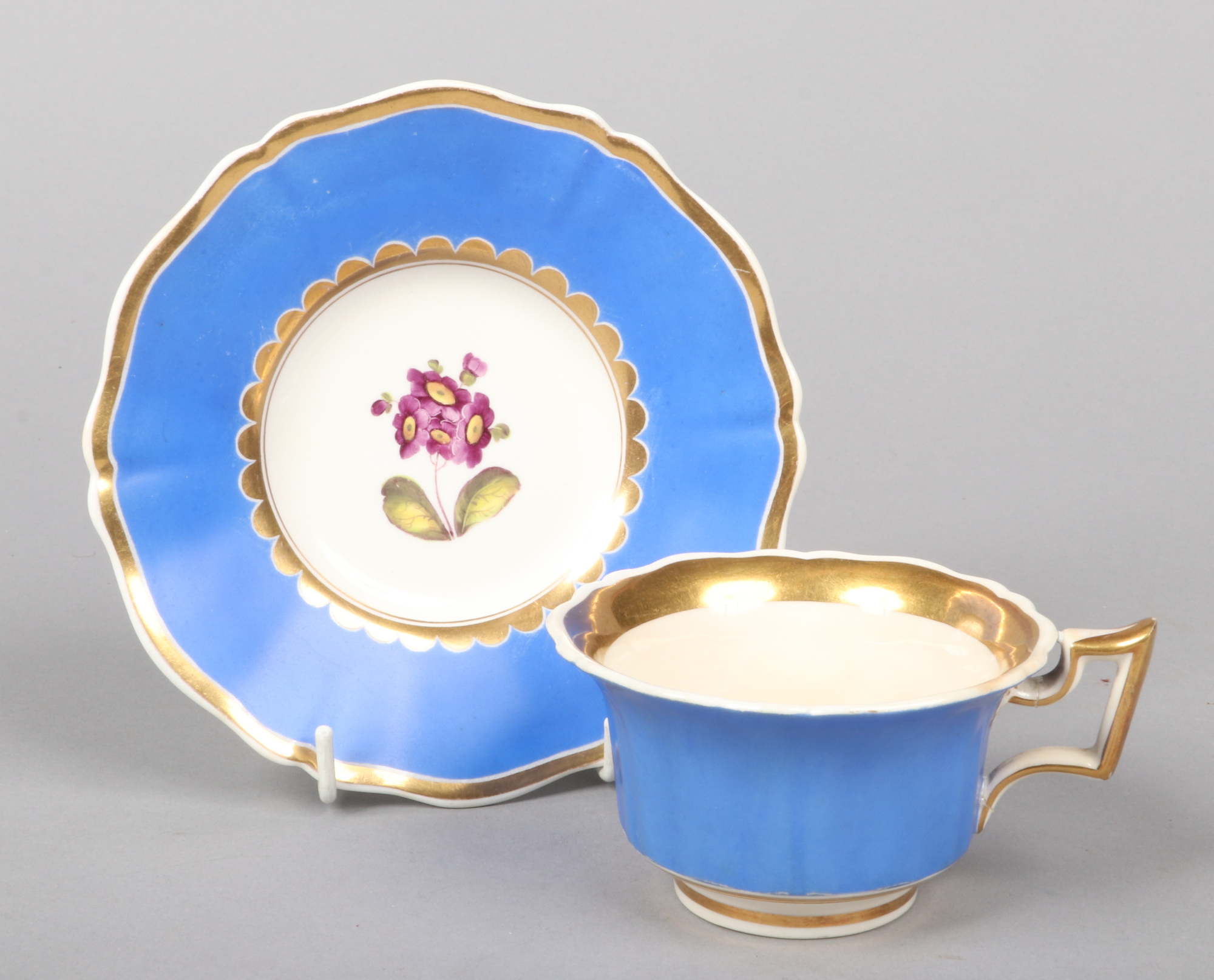 A Rockingham teacup and saucer with square handle, gilded, having blue grounds and painted with