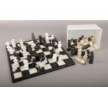 A hand carved onyx black and white chess board, along with two full sets of chess pieces. Two pieces