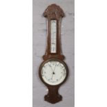 A carved oak banjo barometer with ceramic dial. Crack to thermometer and surround.