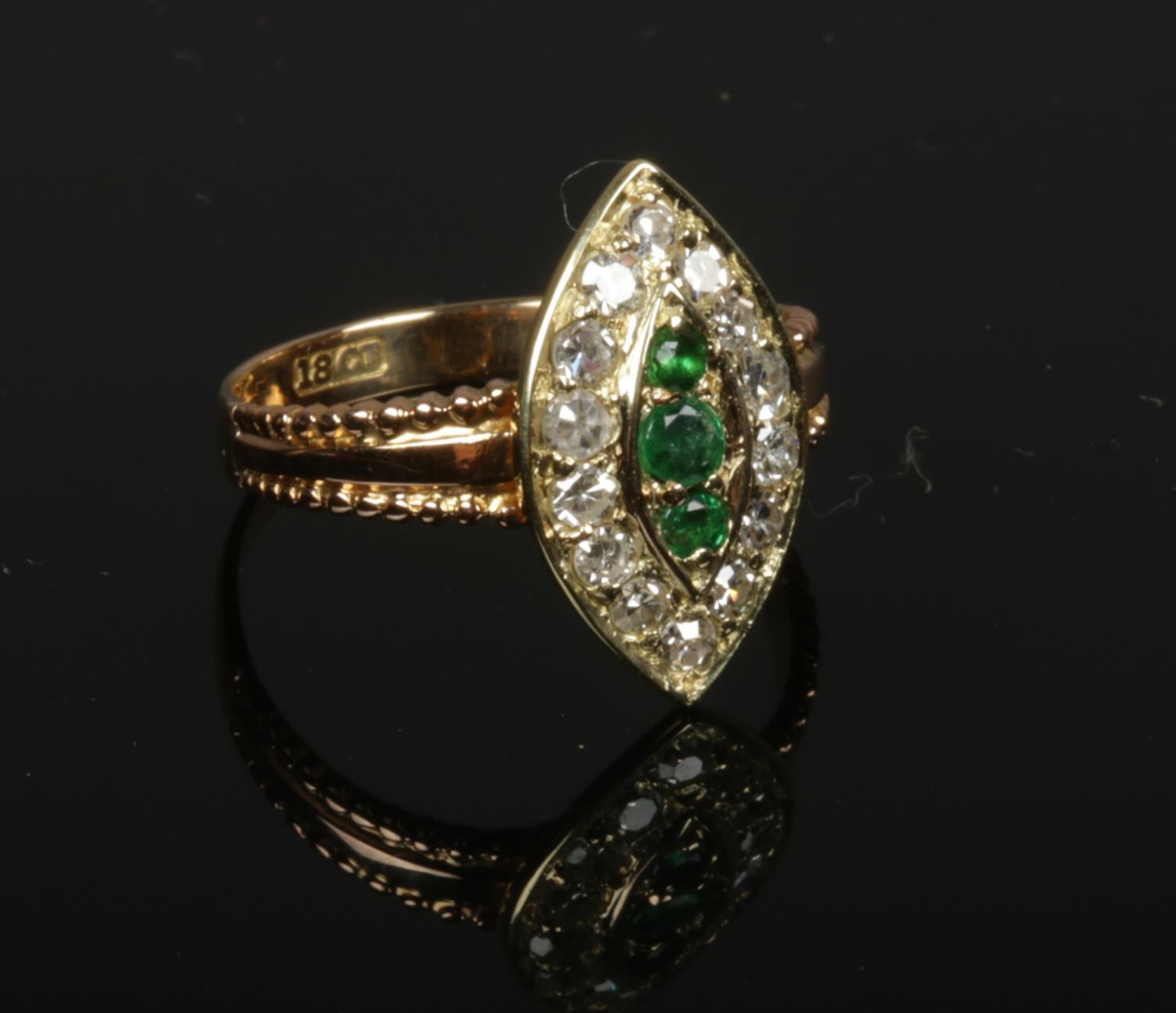 An 18ct gold emerald and diamond cluster ring set on a navette shaped panel. 3 grams gross weight,