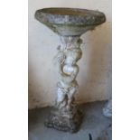 A cast concrete bird bath, the support formed as a cherub.