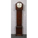 A carved oak granddaughter clock with silvered dial, chiming on a coiled gong.