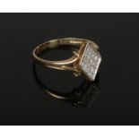 A 9ct gold diamond cluster ring. Set upon a diamond shaped panel between splits shoulders. 2.6 grams