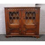 A carved oak lead glazed bookcase with cupboard base. (Height 99cm, Width 110cm, Depth 33cm).